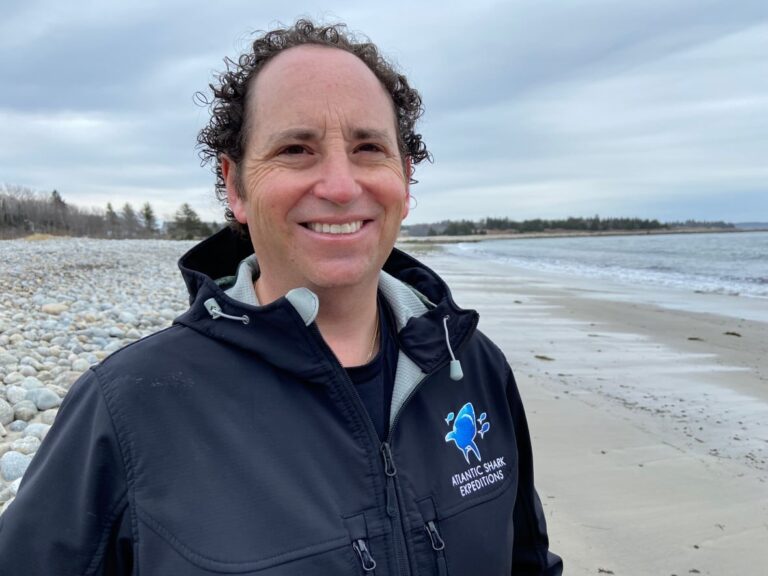 Dr. Neil Hammerschlag standing on a Nova Scotia beach wearing an Atlantic Shark Expeditions jacket.
